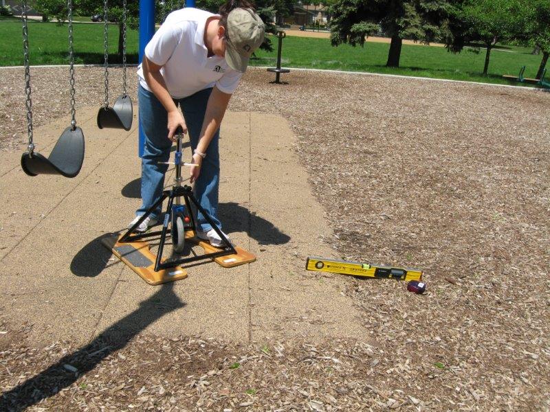 A researcher uses a rotational penetrometer on a playground surface of tiles and engineered wood fiber.