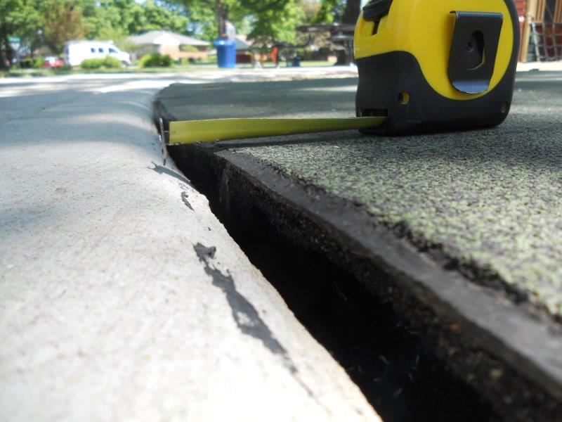 A close-up of a gap between the concrete and rubber surface is shown with a tape measure.