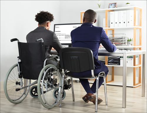 one person sitting in a chair next to a person in a wheelchair at a computer